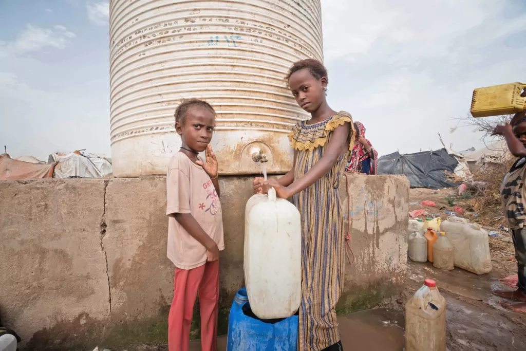 Two girls fill a jerry can at a water tank